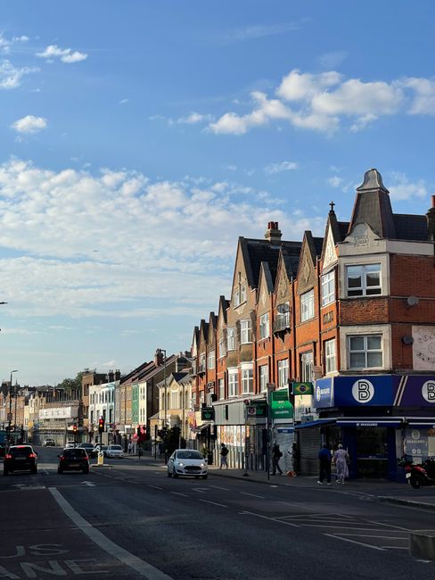 An aerial view of a busy city street in Haringey, showing multiple lanes of parked and moving vehicles including cars, vans, and a double-decker bus, with pedestrians walking on the sidewalks. Surroun