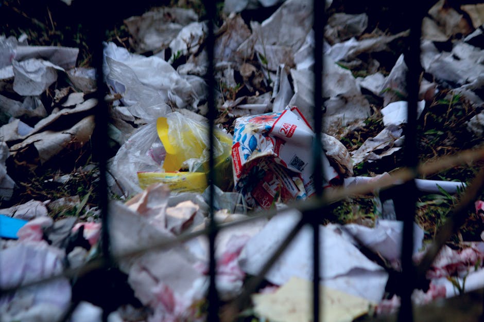 Several blue garbage bags filled with household waste are placed on the concrete steps outside a building near a metal door with a handle and locking mechanism. The building wall is textured and grey,
